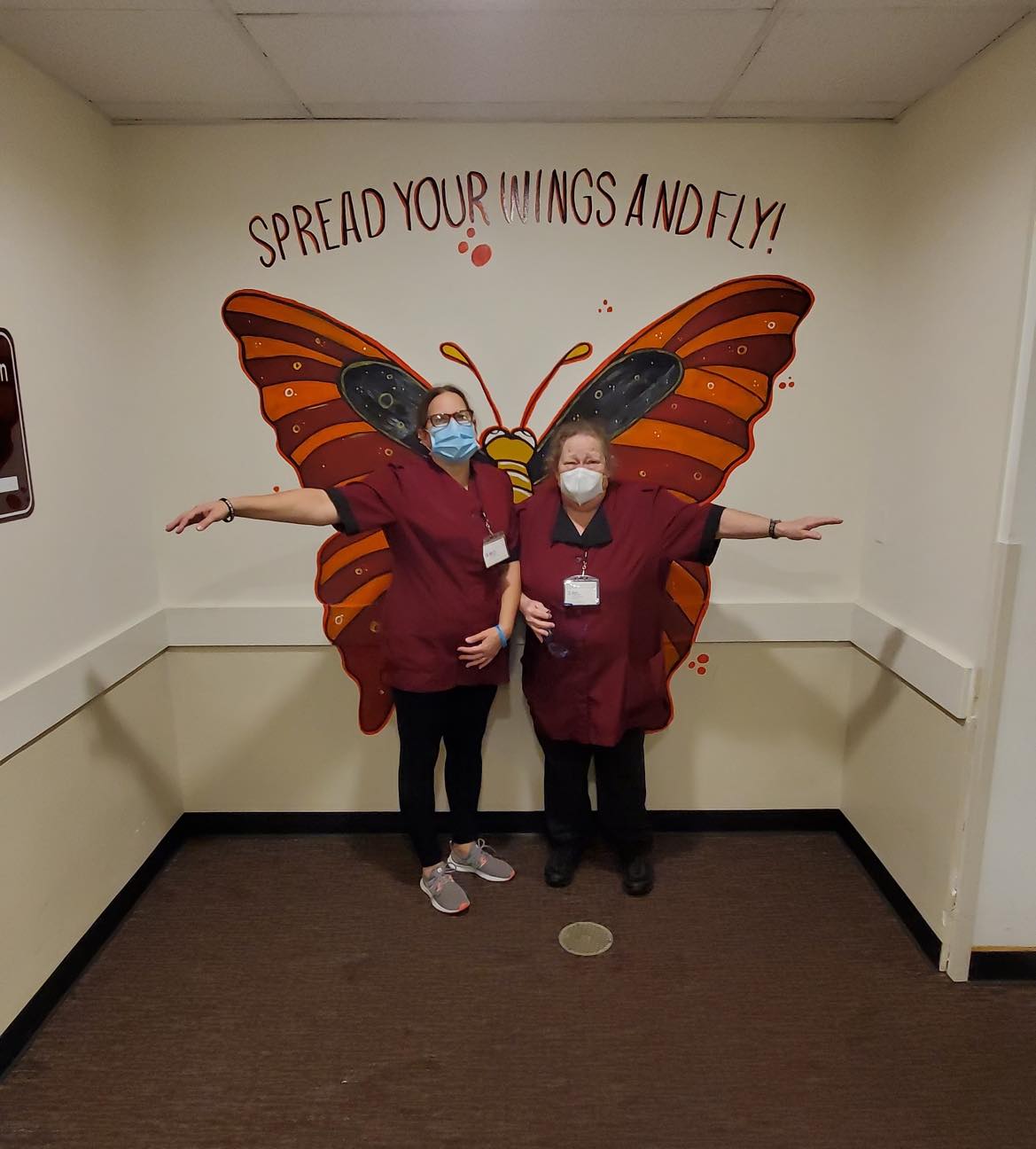 Two Redstone team members posing in front of a butterfly mural